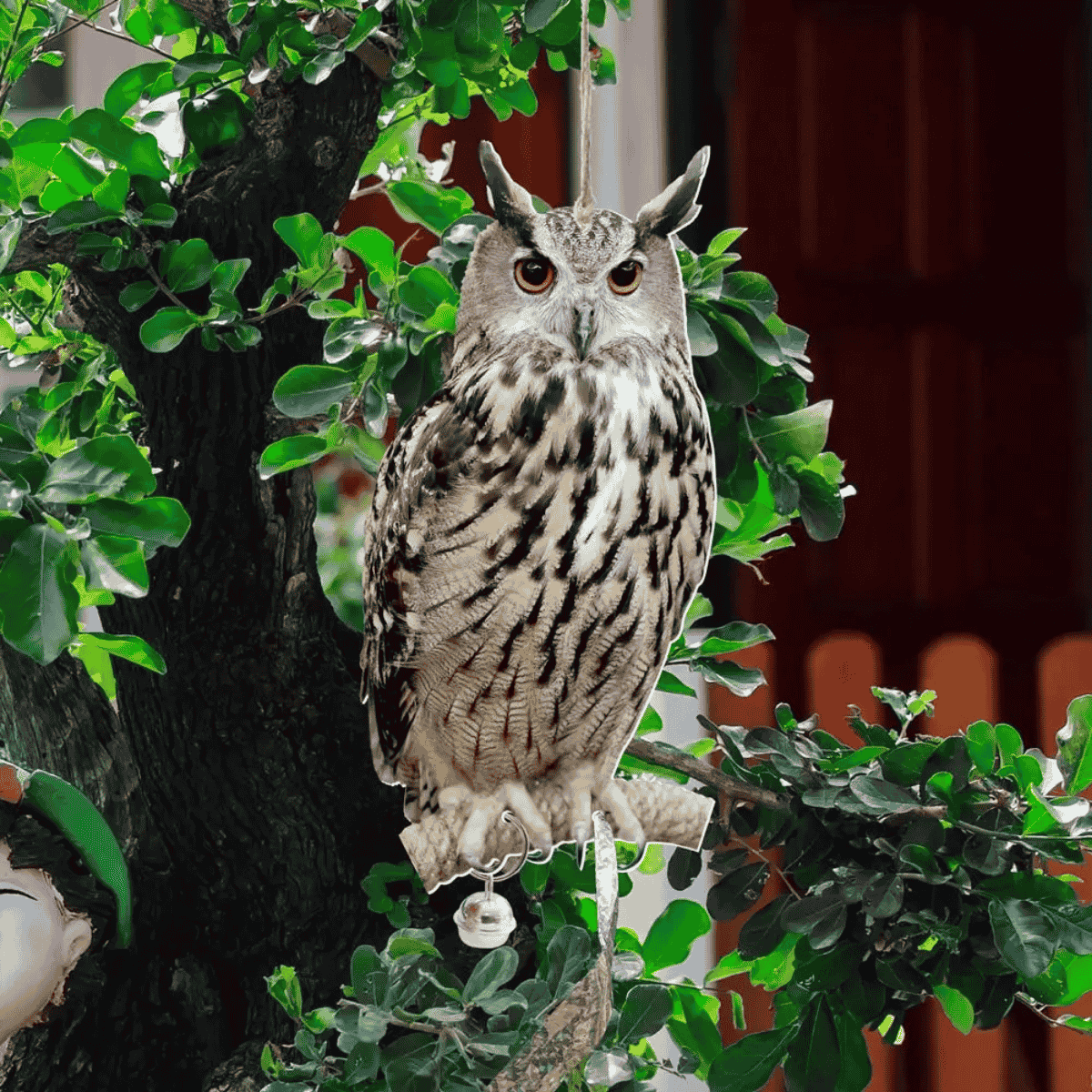 Owl decoy perched on a branch with green leaves and a blurred background