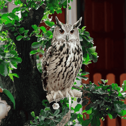 Owl decoy perched on a branch with green leaves and a blurred background